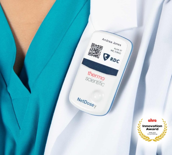 A person wearing a teal medical scrub top and a white coat has a digital whole body monitoring badge labeled "Thermo Scientific NetDose" clipped to their chest, displaying a QR code and the name Andrea Jones for whole body monitoring. In the bottom right corner, the red and gold AHRA Innovation Award logo: a gold laurel wreath surrounds the text "AHRA Innovation Award AHRA 2025 Annual Meeting."