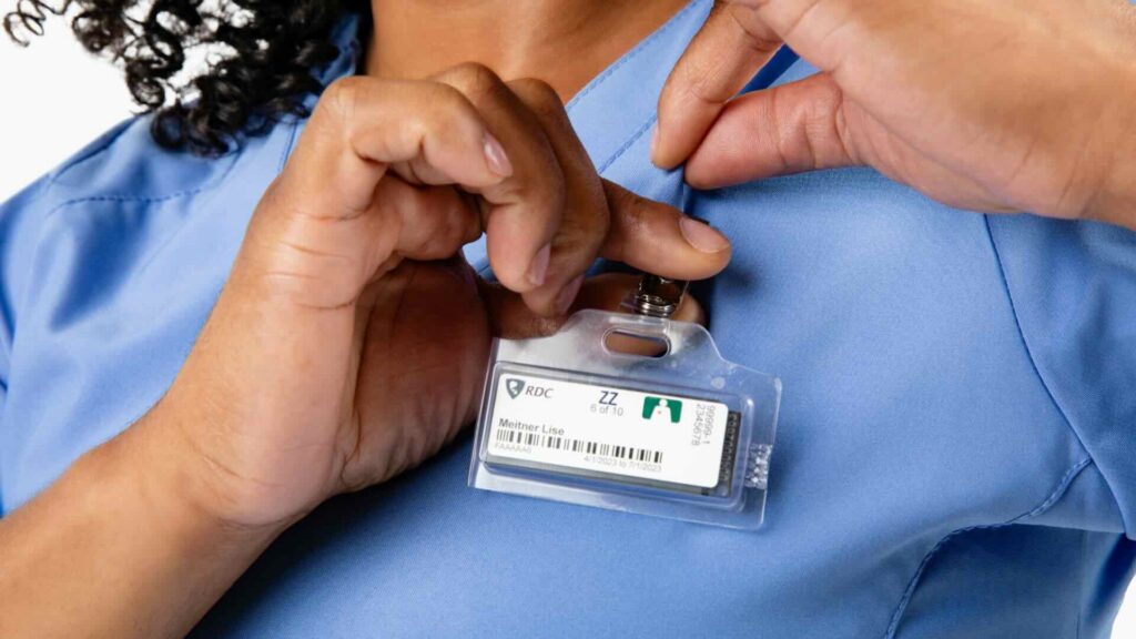 A woman clips an OSL dosimeter to her light blue scrubs.