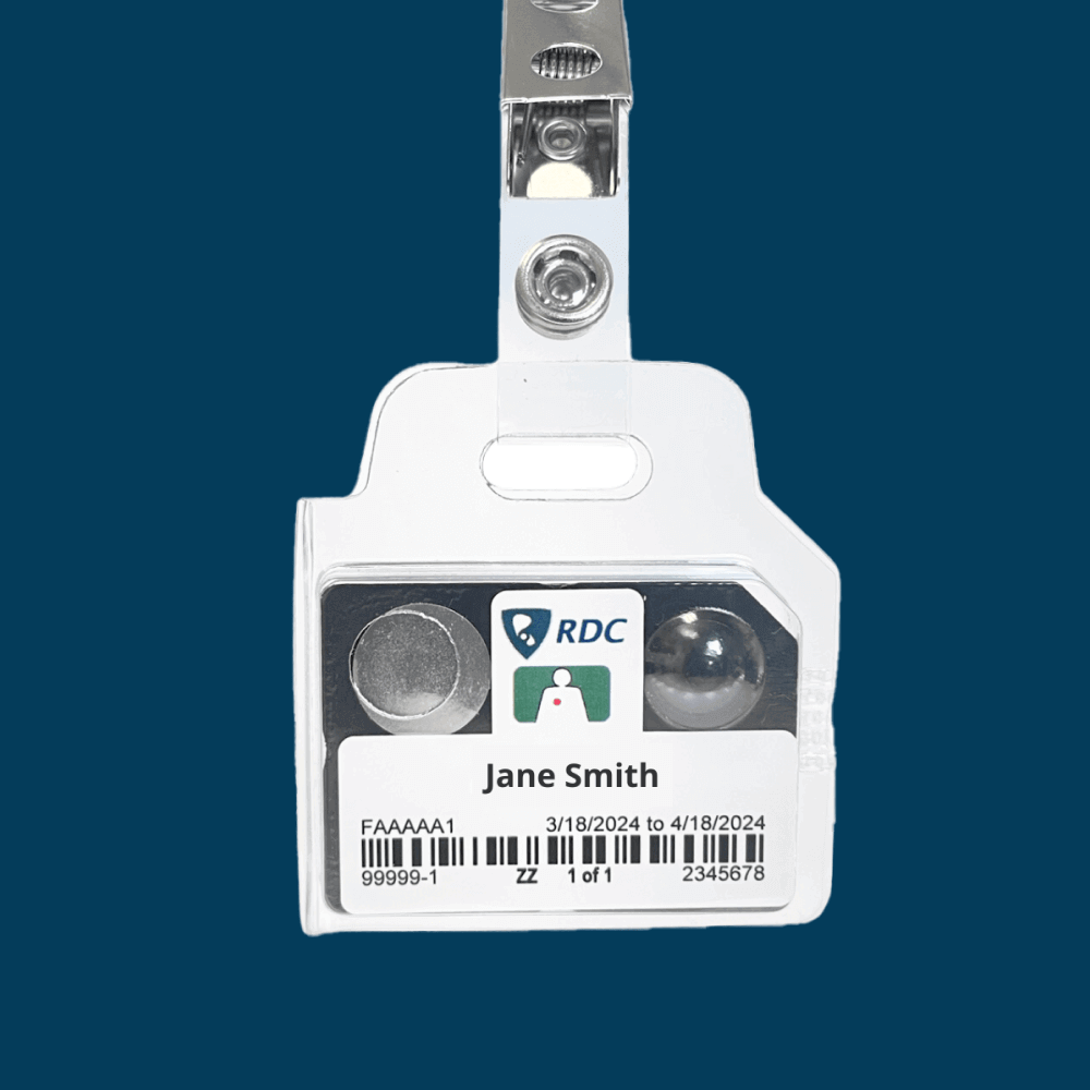 Plastic ID badge and OSL dosimeter with a clear holder displaying the name Jane Smith. It features an RDC logo and barcodes. Dates 3/18/2024 to 4/18/2024 are shown. The badge is clipped to a strap against a blue background.